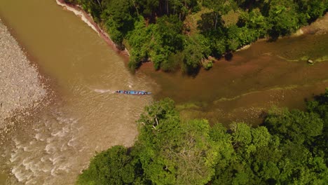 A-traditional-boat-navigating-the-muddy-waters-of-a-river-in-oxapampa,-peru,-surrounded-by-lush-greenery,-aerial-view
