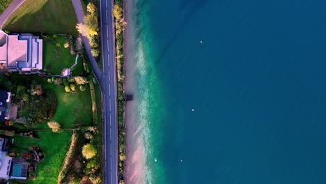 Scenic-aerial-view-of-a-winding-road-lined-with-trees,-leading-to-a-blue-lake