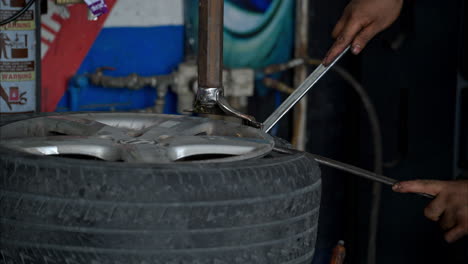 Slow-motion-of-a-male-latin-hispanic-mechanic-using-metal-tools-to-unfit-a-worn-out-and-used-tyre-from-a-very-dirty-wheel