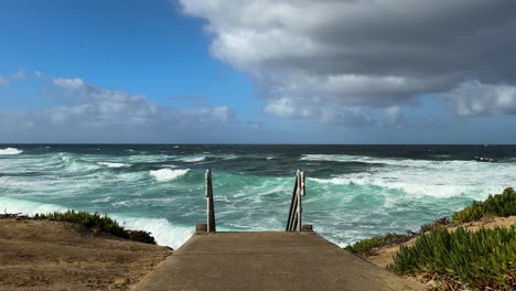 Stairs-leading-down-to-ocean-on-a-beautiful-day-with-waves-and-blue-green-water