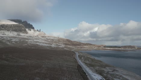 Kurvenreiche-Straße-In-Der-Nähe-Der-Skye-Bridge-Mit-Malerischer-Aussicht-Auf-Die-Gegend-Von-Vail-In-Schottland,-Eine-Mischung-Aus-Schneebedeckten-Hügeln-Und-Klarem-Wasser