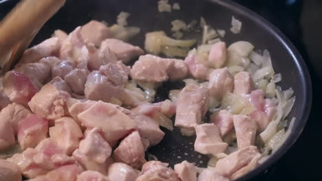 Chicken-and-onions-sauteed-in-hot-frying-pan,-stirred-with-wooden-fork