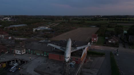 Lapso-De-Tiempo-Aéreo,-Avión-Boeing-707-Abandonado-En-El-Edificio-De-La-Expo-Gowalt-En-El-Crepúsculo,-Wetteren,-Bélgica