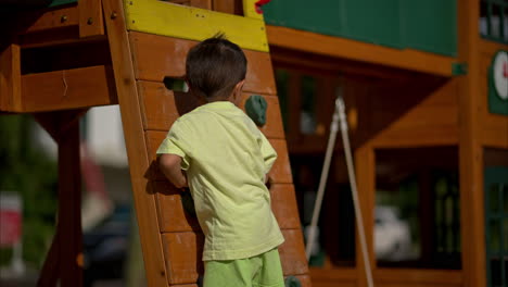 Slow-motion-of-a-young-latin-boy-on-a-climbing-wall-at-a-wooden-playground-on-a-sunny-afternoon