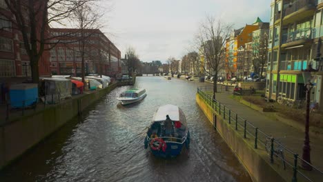 Barco-Por-El-Canal-Con-Turistas-Inclinados-Hacia-Arriba-Desde-El-Río-Hasta-Amsterdam-Stopera-Y-Waterlooplein