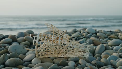 Discarded-Fish-Trap-on-Pebble-Beach,-trash-on-the-beach