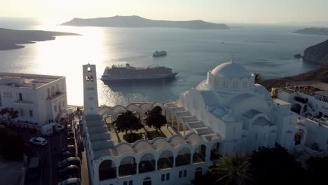 Aerial-over-Orthodox-Cathedral-of-Fira-Revealing-Old-Harbor-Bay-Cruises,-Santorini,-Greece