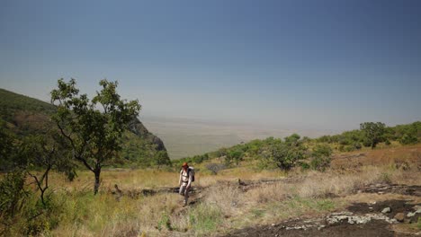 A-western-hiker-climbs-along-a-mountain-top-in-the-hot-sun-in-East-Africa-with-great-views