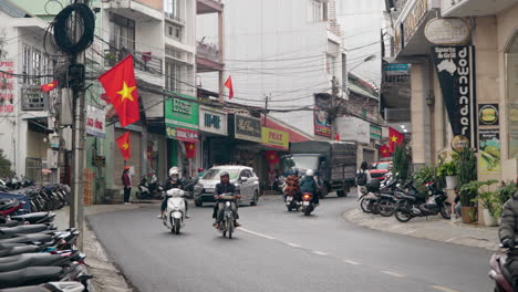 Urban-Dalat-City-Street-Traffic-with-Many-People-Riding-Motorbikes-and-Vietnamese-Flags-Hanging-on-Building-Facades