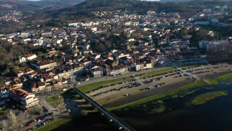 Footbridge-across-river-leads-to-Ponte-de-Lima-Town,-the-oldest-village-in-Portugal,-panoramic-aerial-establish-at-golden-hour