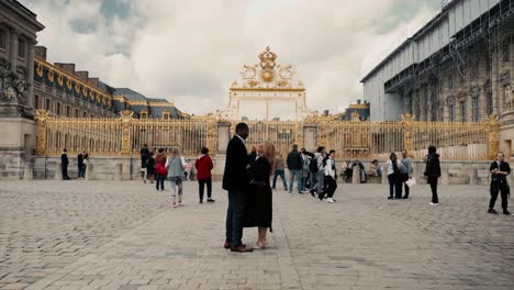 Gemischtrassiges-Paar-Vor-Dem-Berühmten-Schloss-Versailles,-Dem-Goldenen-Hauptschloss-Der-Ehre,-In-Paris,-Frankreich,-Kuschelnd-Und-Flirtend-An-Einem-Bewölkten-Frühlingstag-–-Filmreife-Weitwinkelaufnahme