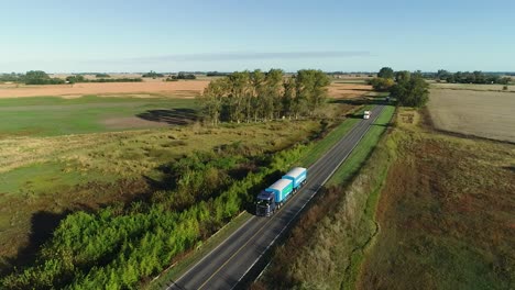 Aerial-shot-of-trucks-driving-along-a-rural-highway-on-a-sunny-day,-casting-long-shadows