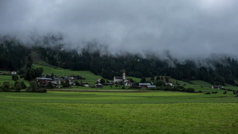 Fog-flowing-over-typical-township-in-Dolomites-with-church-tower,-time-lapse