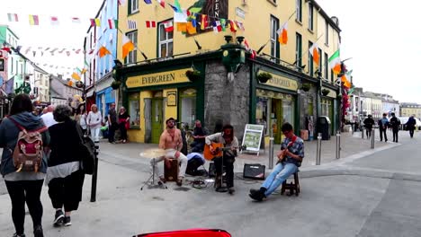 Street-musicians-playing-in-Quay-St-with-national-flags-over-them,-Galway