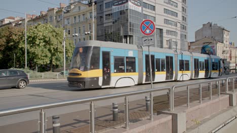 Modern-tram-driving-through-city-handheld-pan-right,-summer-day,-busy-morning