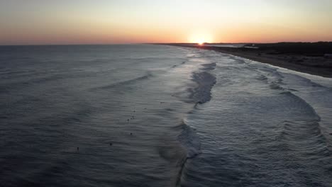 Aerial-view-of-surfers-in-the-ocean-at-sunset,-waiting-for-waves-on-a-tranquil-evening