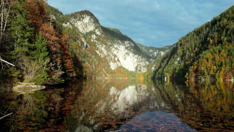 Die-Feurige-Umarmung-Des-Herbstes-Malt-Die-Berge-Rund-Um-Einen-Ruhigen-See,-Wo-Bunte-Blätter-Auf-Der-Wasseroberfläche-Pirouetten-Drehen