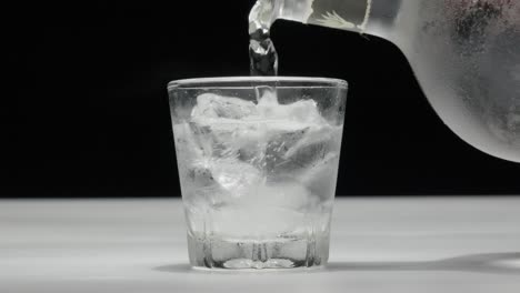 Close-up-of-a-drink-being-poured-over-ice-cubes-in-a-glass,-against-a-dark-background