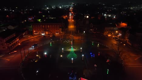 Aerial-night-view-of-a-roundabout-with-a-lit-Christmas-tree-and-colorful-festive-lights-in-an-American-town