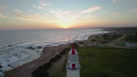 Sunset-view-of-Farol-lighthouse-in-Portugal-with-ocean-waves-and-coastal-landscape,-aerial-view