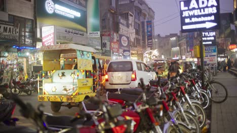 Belebte-Straßenszene-In-Gujarat,-Pakistan-Mit-Motorrädern,-Rikschas-Und-Geschäftigem-Abendpublikum