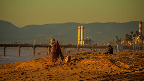 -Manhattan-Beach,-California-at-sunset-with-a-bridge,-refinery,-and-mountains-in-the-background