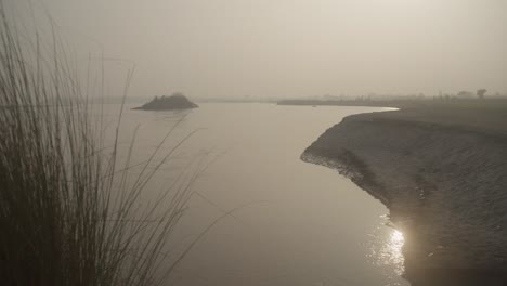Sunrise-over-River-Ghanab-with-gentle-water-flow,-tall-grass-in-foreground,-tranquil-morning-scene