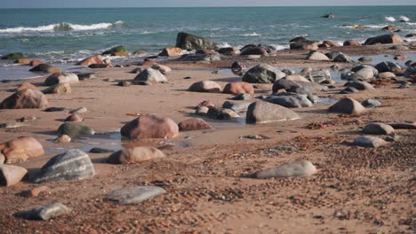 Stones-and-pebbles-cover-the-sandy-beach-as-waves-roll-slowly-in-the-background