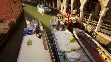 Logistik-In-Venedig:-Mann-Verlädt-Waren-Von-Einem-Boot-Zum-Anderen,-Um-Sie-An-Geschäfte-Und-Menschen-In-Der-Historischen-Stadt-Zu-Liefern