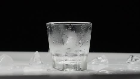 Gefrorenes-Eis-Fällt-In-Ein-Nasses-Glas-Auf-Einem-Weißen-Tisch