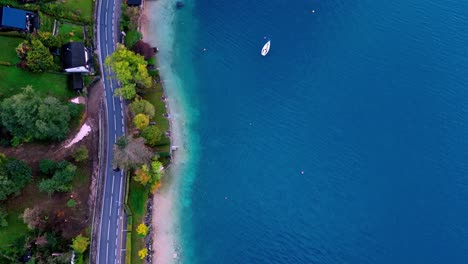 Aerial-view-of-a-winding-road-along-a-lake,-with-a-lone-boat-anchored-in-the-still-water