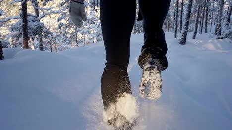 Person-hiking-through-snow-in-forest,-snow-chains-on-boots
