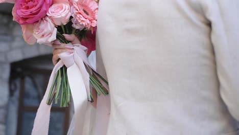bride-holds-pink-wedding-bouquet-hugging-groom-in-beige-suit,-closeup-slow-motion