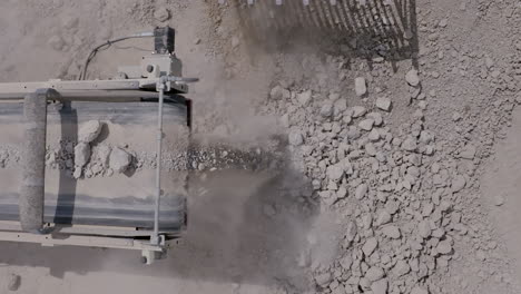 Top-down-aerial-footage-of-a-cement-crusher-dropping-rocks-into-a-pile-that-a-small-bulldozer-is-picking-up
