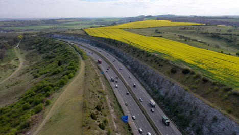Aerial-wide-shot-over-UK-M3-motorway-built-through-hillside-and-rapeseed-fields