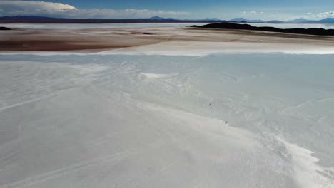 Very-tiny-people-walk-on-vast-salt-flat-at-Uyuni,-Bolivia,-aerial-view
