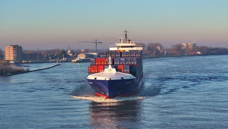 Parallax-Drohne-Mit-Schwenkaufnahme-Eines-Voll-Beladenen-Frachters,-Der-über-Einen-Schmalen-Fluss-Segelt