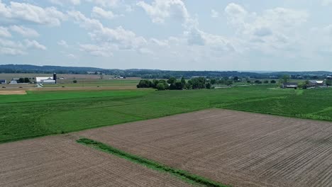 Una-Rotación-Aérea-Y-Lenta-De-Tierras-De-Cultivo,-Con-Campos-Verdes-Y-Campos-Arados-En-Un-Día-Parcialmente-Soleado.