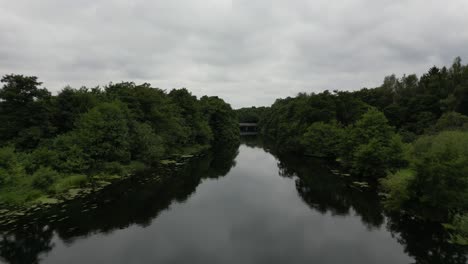 Drohnenaufnahme-Des-Flusses-Gudenå,-Bei-Der-Die-Drohne-über-Und-Entlang-Des-Flusses-Auf-Dem-Weg-Zu-Einer-Kleinen-Brücke-Fliegt