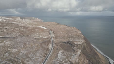 A-coastal-road-along-cliffs-near-the-old-man-of-storr-on-the-isle-of-skye,-scotland,-under-cloudy-skies,-aerial-view