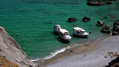 Three-small-boats-with-people-moored-at-a-deserted-exotic-beach-,-people-swimming