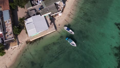 Aerial-top-down-view-of-coastal-fishing-village-with-vessel,-pier,-harbour-and-airport,-Caribbean-island