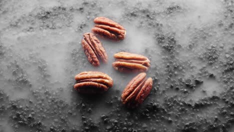 5-crispy-pecan-nuts-are-being-roasted-on-a-bed-of-hot-black-rocks,-clouds-of-steam-flow-around-them