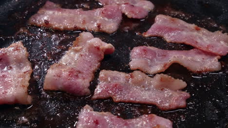 Fatty-bacon-strips-shrink-as-they-cook,-sizzle-in-hot-frying-pan