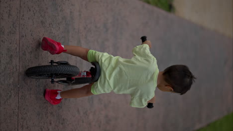 Vertical-slow-motion-of-a-young-little-latin-boy-riding-a-training-bike-on-a-warm-afternoon