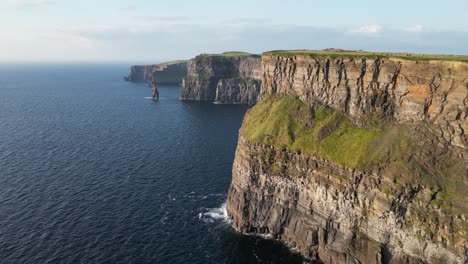 The-cliffs-of-moher-in-ireland,-majestic-natural-wonder,-blue-ocean-below,-bright-sunny-day,-aerial-view
