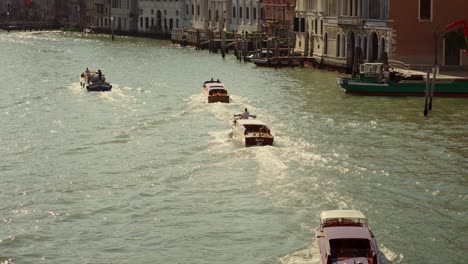 Taxi-boat-on-the-water-of-Canal-Grande-in-Venice,-Italy,-is-cruising-under-a-bridge-in-the-morning-sunlight