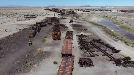 Aerial-flight-to-tourists-exploring-train-graveyard-at-Uyuni,-Bolivia