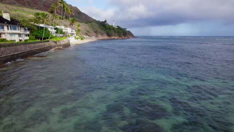 drone-footage-along-the-shore-line-of-Oahu-Hawaii-passing-Diamond-Head-lighthouse-across-the-clear-blue-Pacific-ocean-and-the-sandy-beaches-along-the-steep-cliffs-of-Diamond-Head