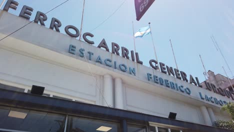 Primer-Plano-De-La-Estación-De-Tren-Urquiza,-Bandera-Argentina-Ondeando-Sobre-El-Horizonte-Azul-Arquitectura-Federico-Lacroze,-Barrio-Chacarita